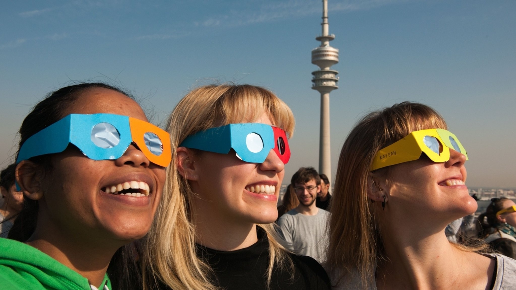 Drei junge Frauen mit Sonnenfinsternis-Schutzbrillen. Blicken Sie niemals ungeschützt ins Sonnenlicht!