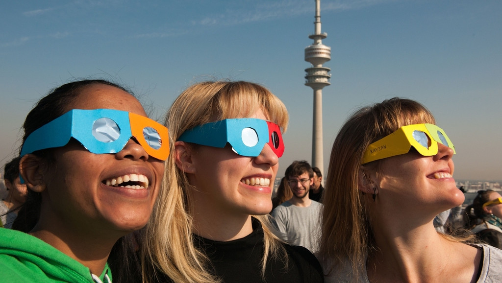 Drei junge Frauen mit Sonnenfinsternis-Schutzbrillen. Blicken Sie niemals ungeschützt ins Sonnenlicht!