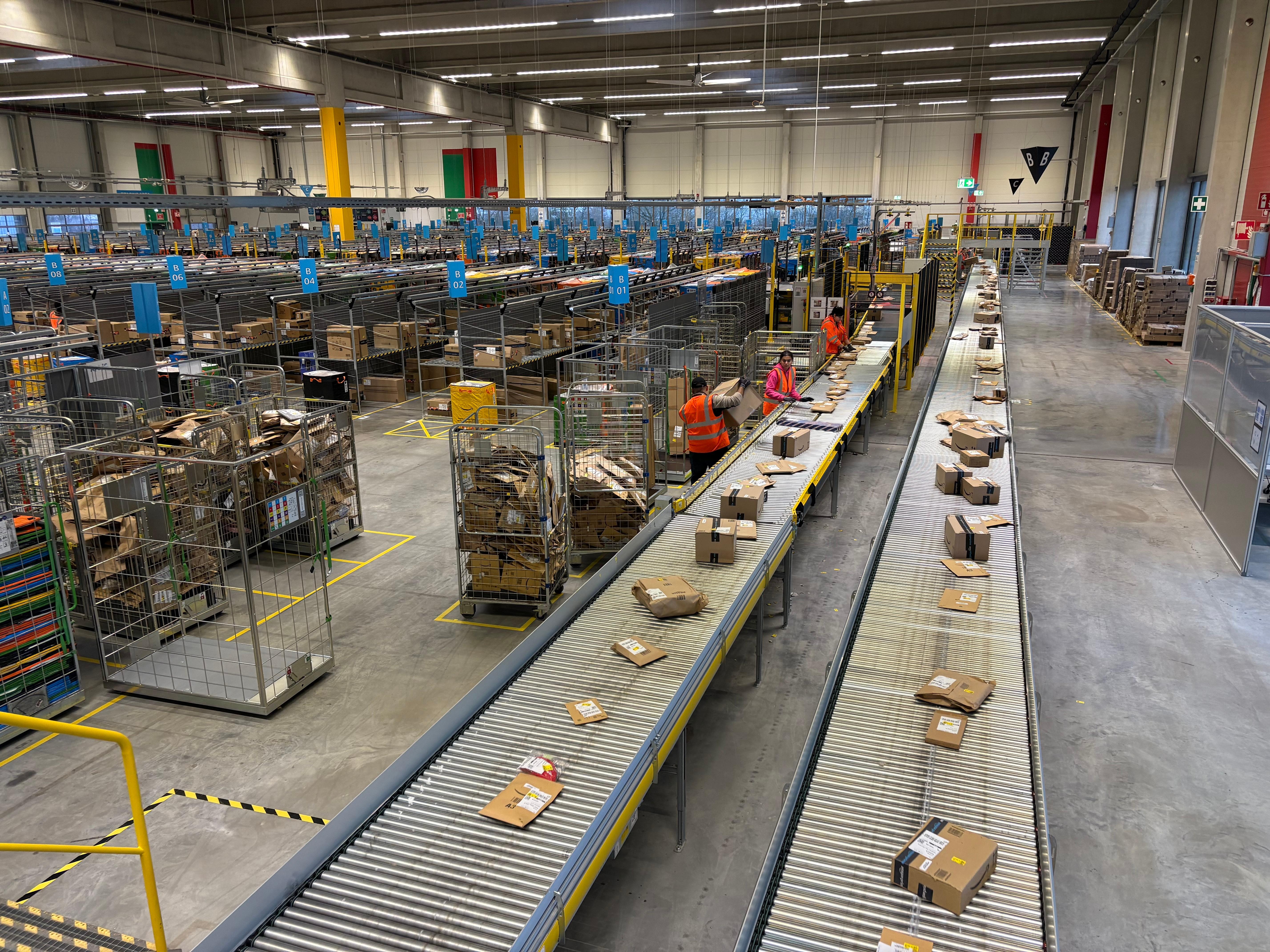 Mitarbeitende des Amazon-Verteilzentrums sortieren Pakete in einer großen Halle