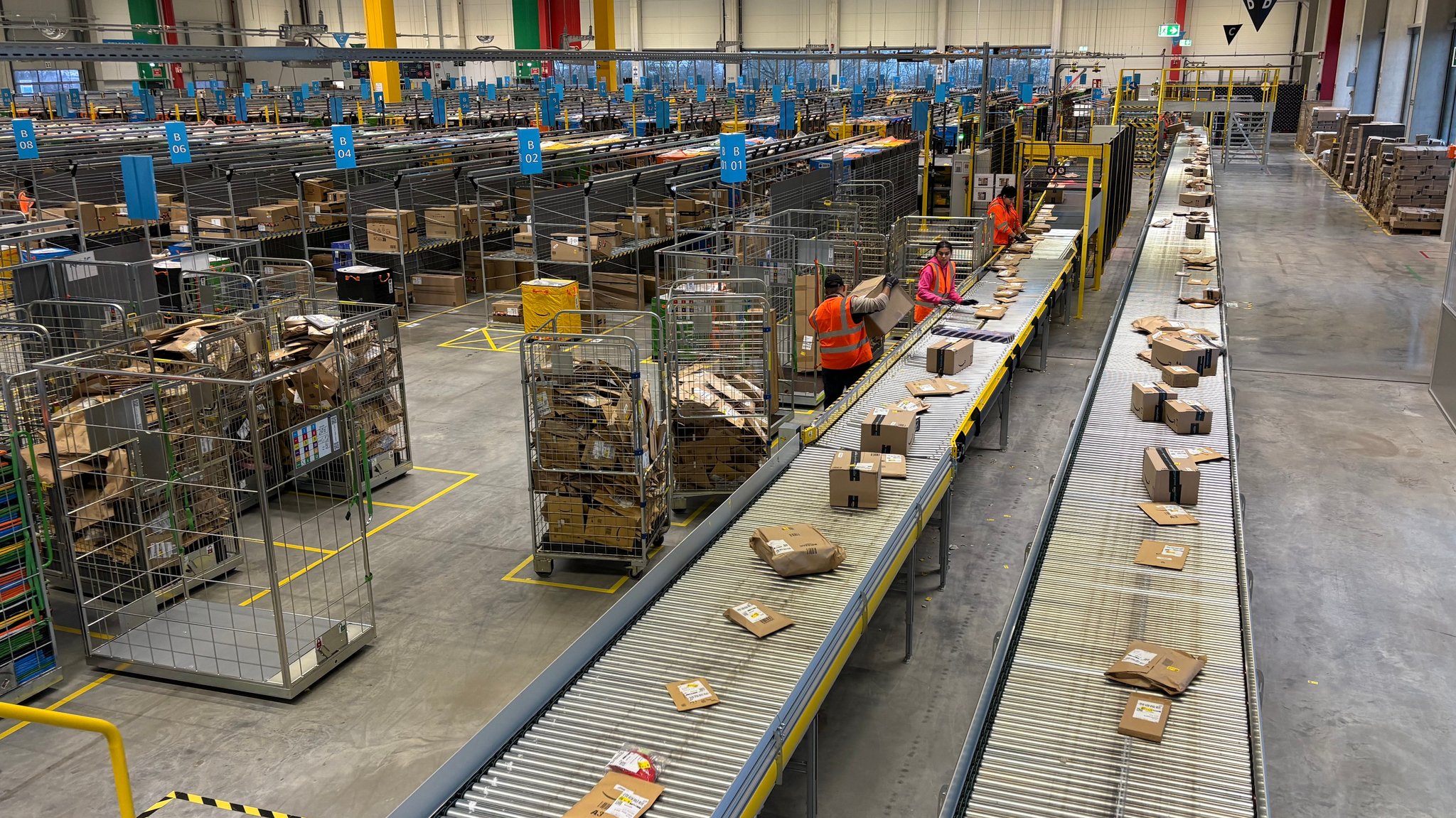 Mitarbeitende des Amazon-Verteilzentrums sortieren Pakete in einer großen Halle