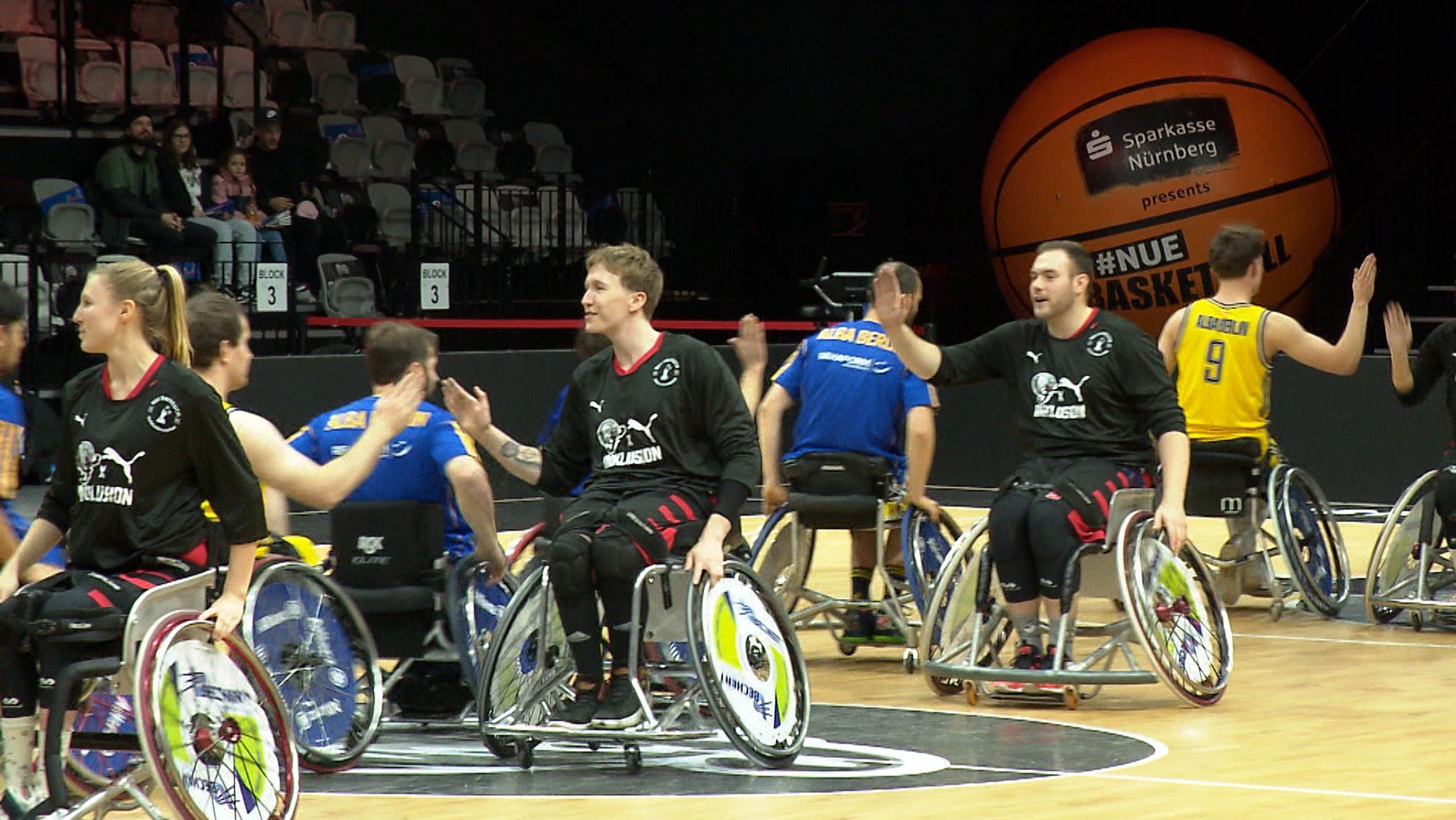 Rollstuhlbasketballer unterwegs auf dem Spielfeld in einer Halle.