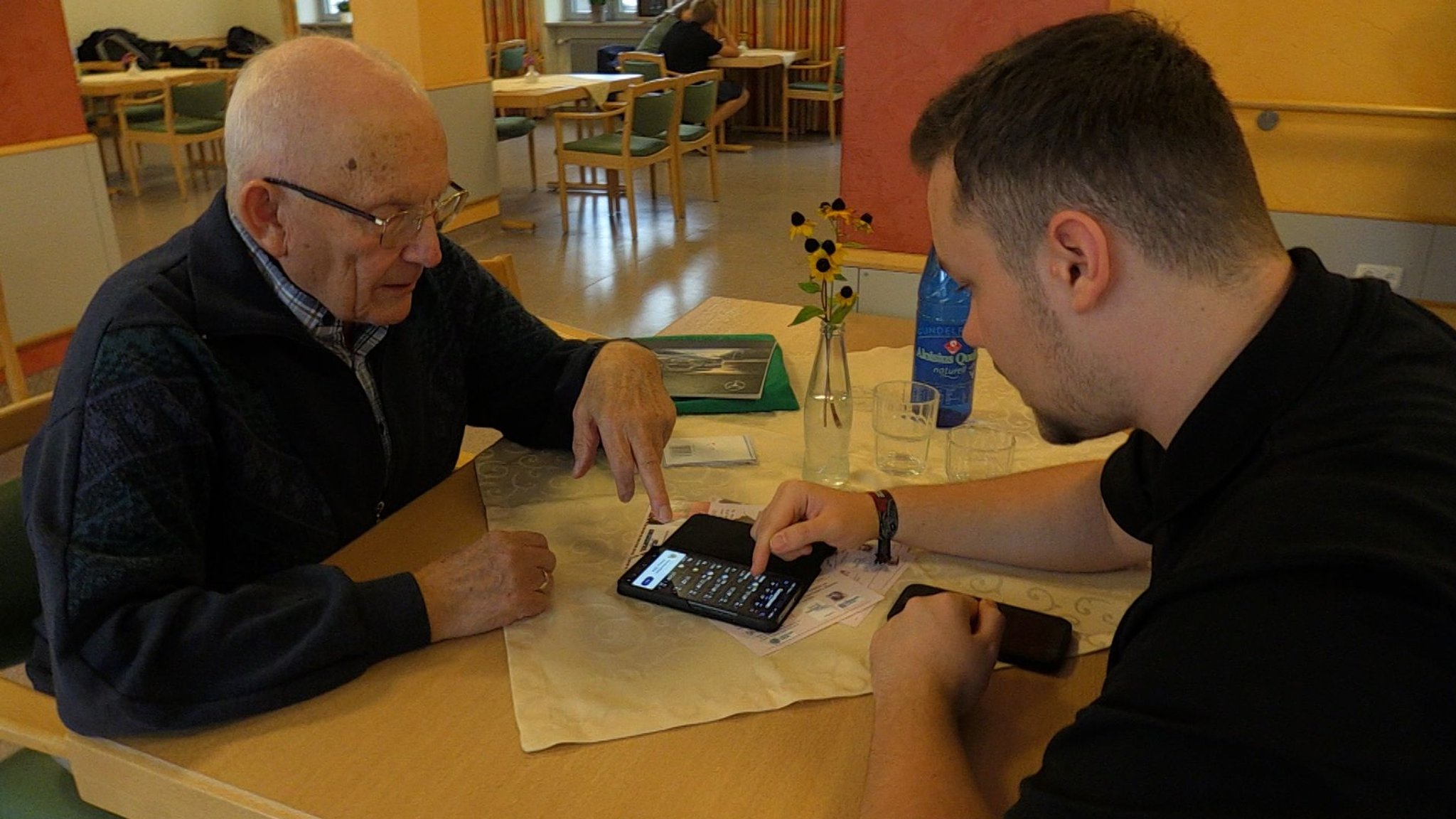 Maxim (rechts) hilft Karl Lechner mit seinem Smartphone. | Bild: BR/Vera Held Maxim (rechts) hilft Karl Lechner mit seinem Smartphone.