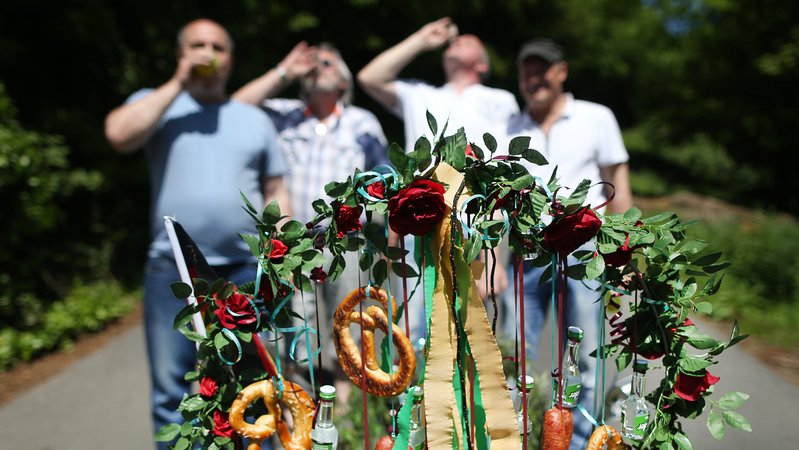 Bollerwagen im Vordergrund. Im Hintergrund (unscharf) Männer, die einen Schnaps trinken | Bild: picture alliance / Ina Fassbender/dpa | Ina Fassbender Bollerwagen im Vordergrund. Im Hintergrund (unscharf) Männer, die einen Schnaps trinken
