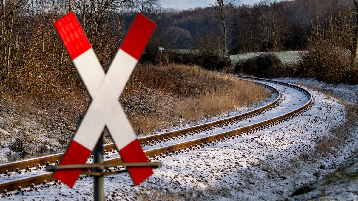 Eine dünne Schneeschicht überzieht die Gleise an einem mit einem Andreaskreuz beschilderten unbeschrankten Bahnübergang (Symbolbild).