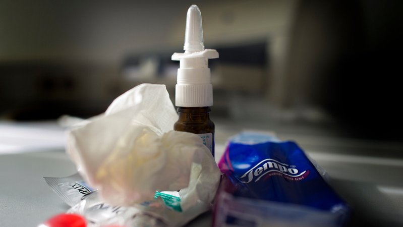 Anti-Erkältungsmittel wie Nasenspray, Halstabletten und Papiertaschentücher liegen auf einem Tisch.