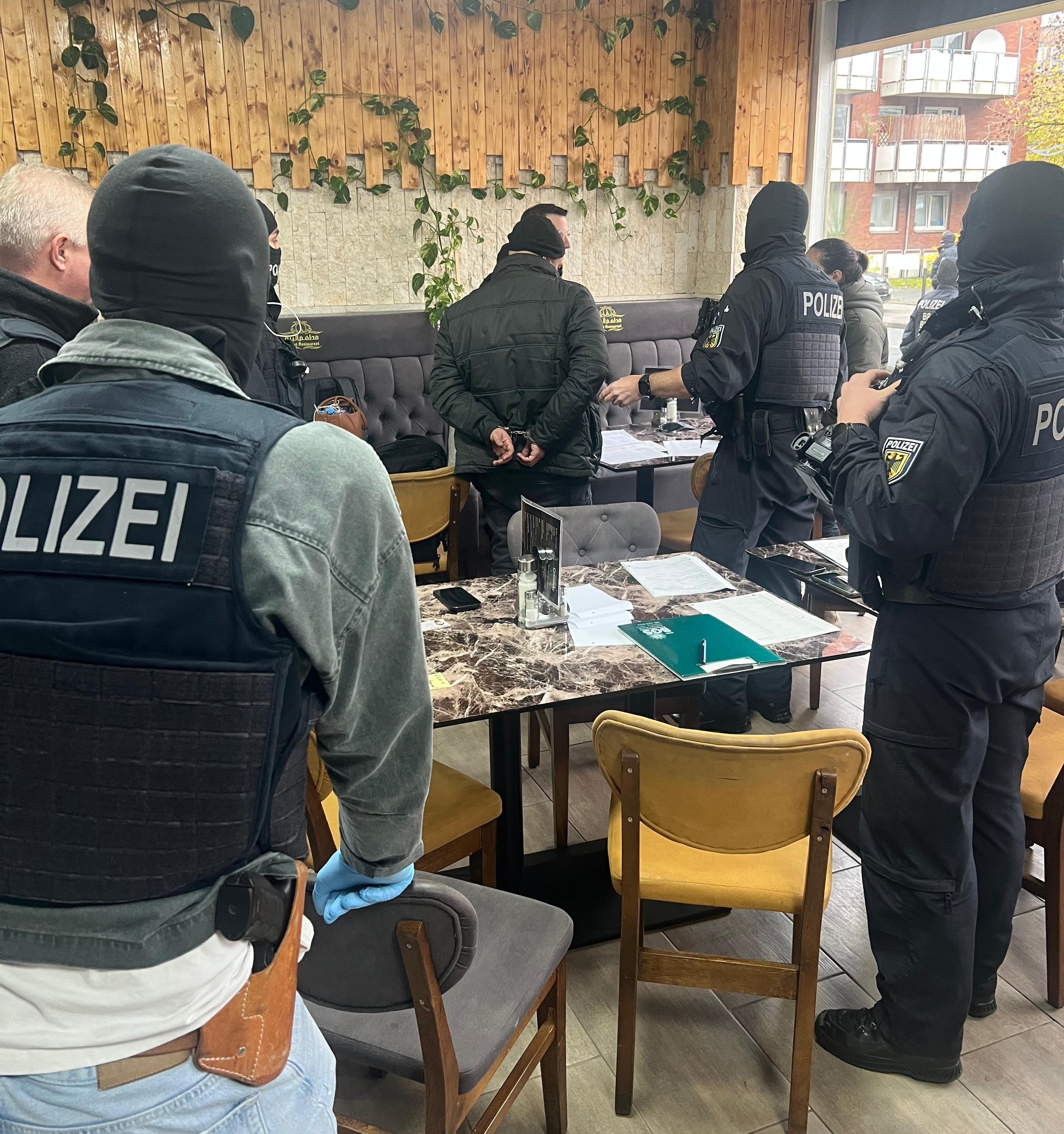 Vermummte Polizisten nehmen in einem Café mutmaßliche Mitglieder einer Schleuserbande fest.