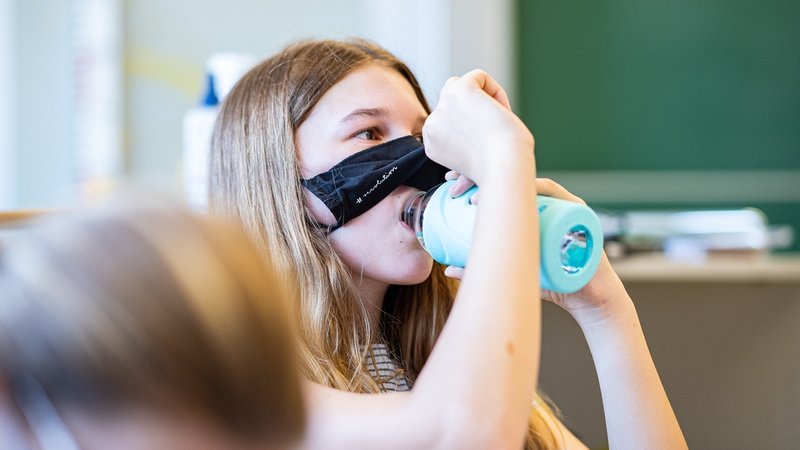 Eine Schülerin der Klasse 8a der Gesamtschule in Münster, hebt ihre Mund- und Nasenmaske an um etwas zu trinken. Das Bundesland Nordrhein-Westfalen startet mit Maskenpflicht nach den Sommerferien wieder in den Regel-Schulbetrieb.