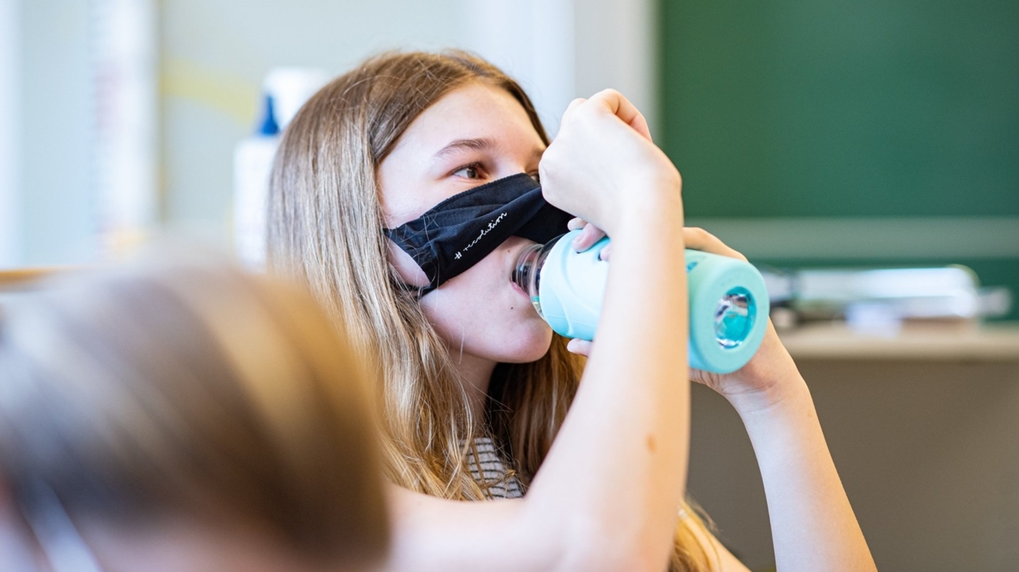 Eine Schülerin der Klasse 8a der Gesamtschule in Münster, hebt ihre Mund- und Nasenmaske an um etwas zu trinken. Das Bundesland Nordrhein-Westfalen startet mit Maskenpflicht nach den Sommerferien wieder in den Regel-Schulbetrieb.