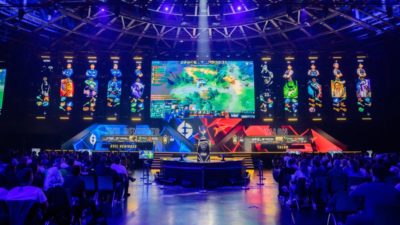 E-Sport: Zweites Major-Turnier des Spiels Dota Pro Circuit 2023 am Finalwochenende. In einer Halle schauen Dutzende Menschen auf mehrere Bildschirme, die hell erleuchtet vor Ihnen an der Wand der Veranstaltungshalle installiert sind. | Bild: picture alliance/dpa/Christoph Soeder E-Sport: Zweites Major-Turnier des Spiels Dota Pro Circuit 2023 am Finalwochenende. In einer Halle schauen Dutzende Menschen auf mehrere Bildschirme, die hell erleuchtet vor Ihnen an der Wand der Veranstaltungshalle installiert sind.