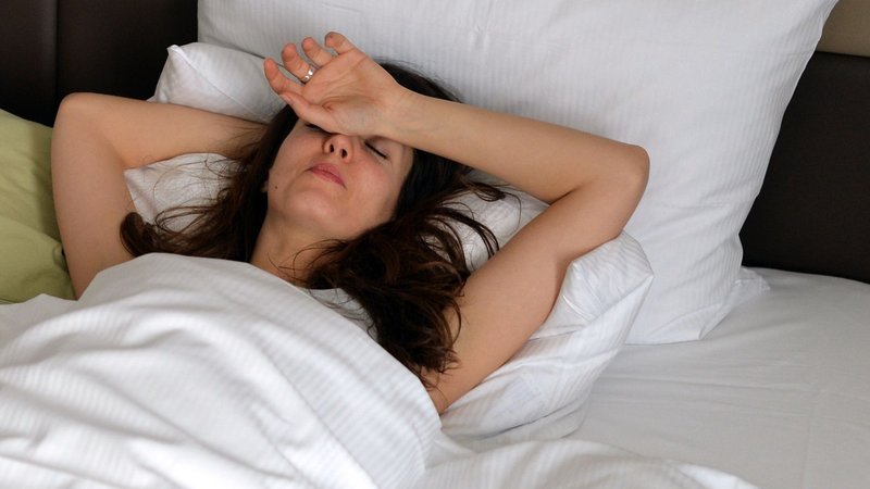 Symbolbild: Frau liegt mit Migräne im Bett