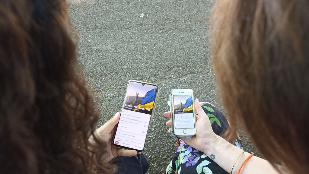Zwei Frauen halten ihre Smartphones in der Hand, darauf die Angebote von 'Ukraine Help Nürnberg'