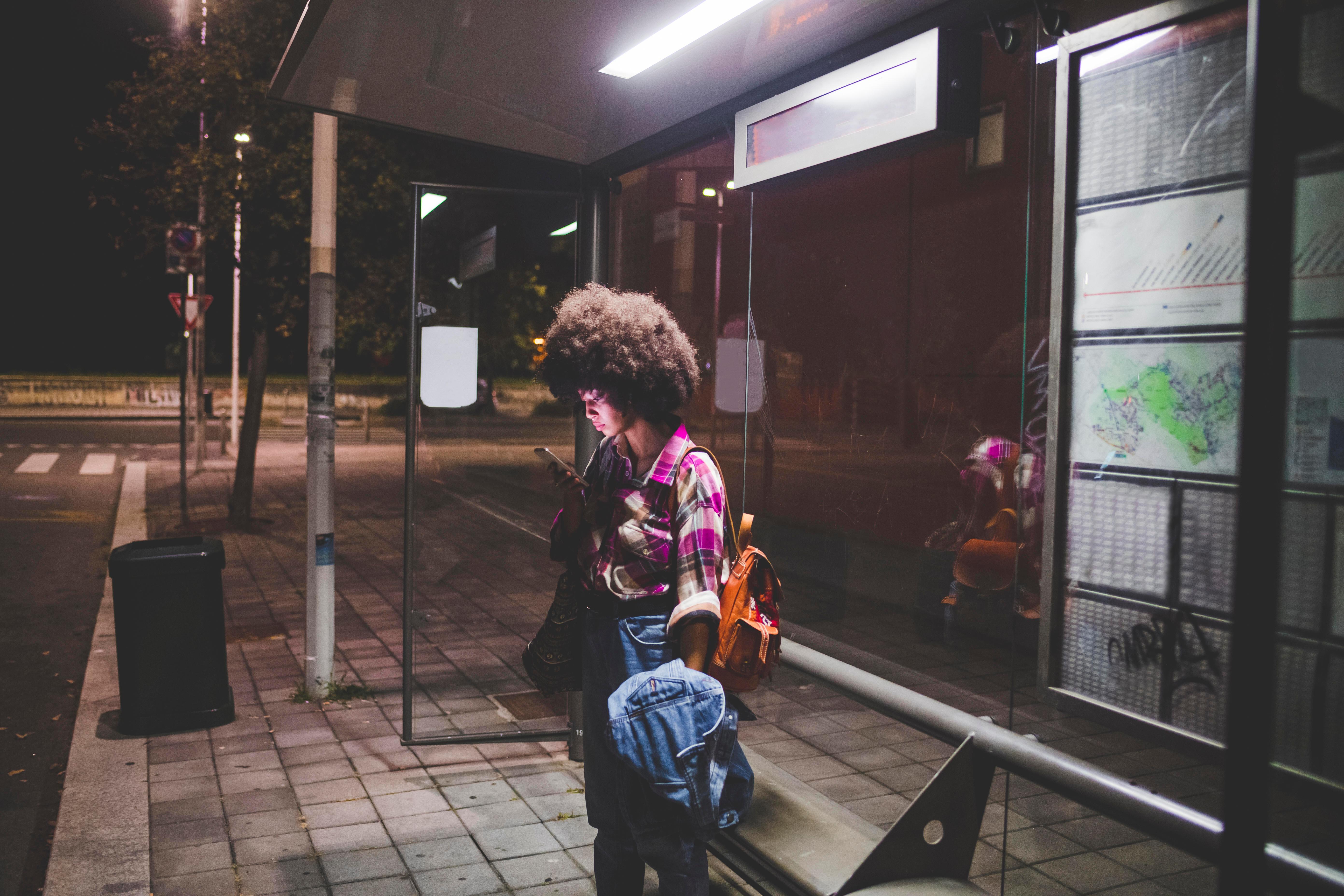 Symbolbild: Eine junge Frau steht nachts an einer Haltestelle 