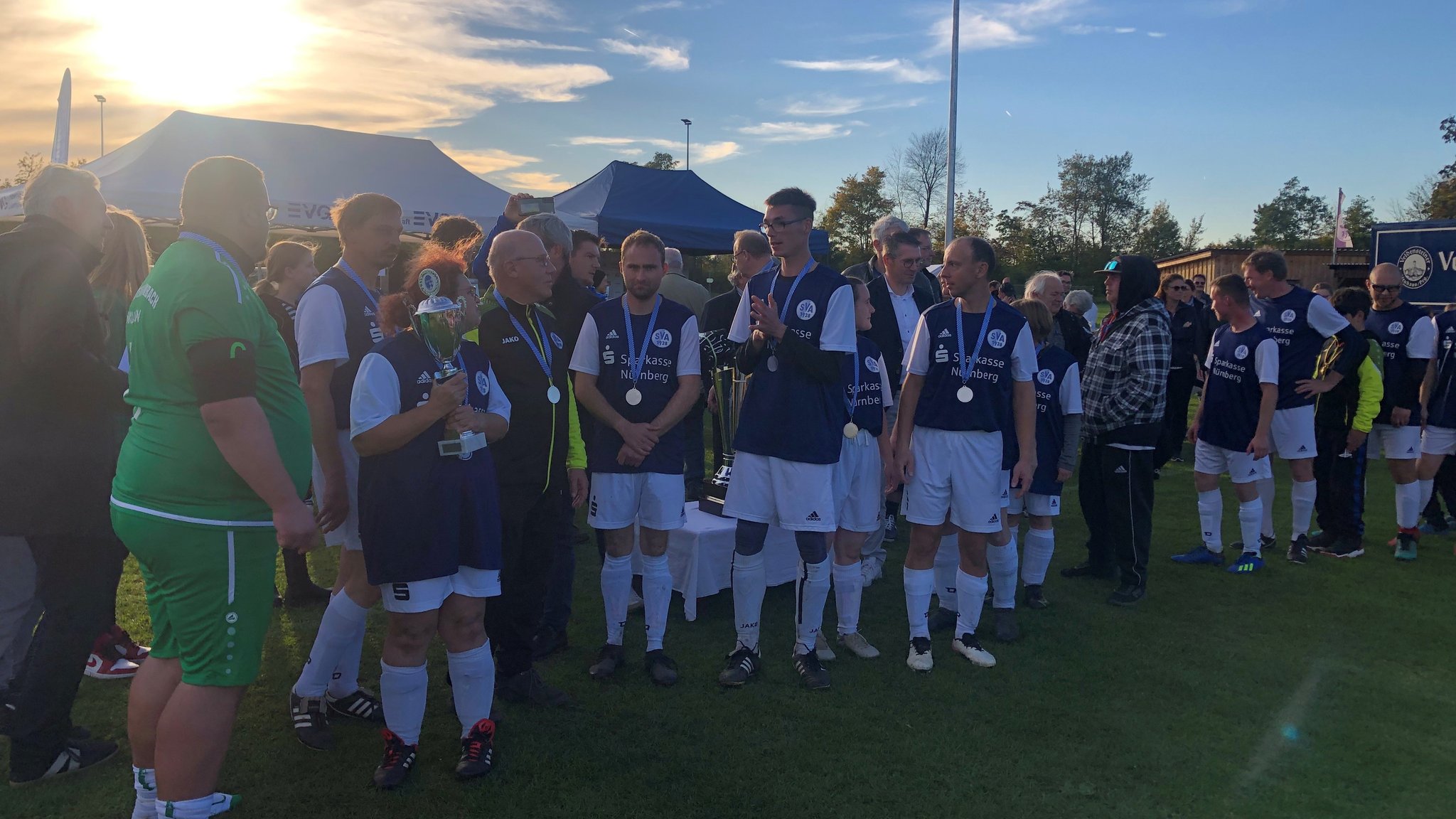 Fußballerinnen und Fußballer im Trikot stehen beisammen in der Abendsonne.