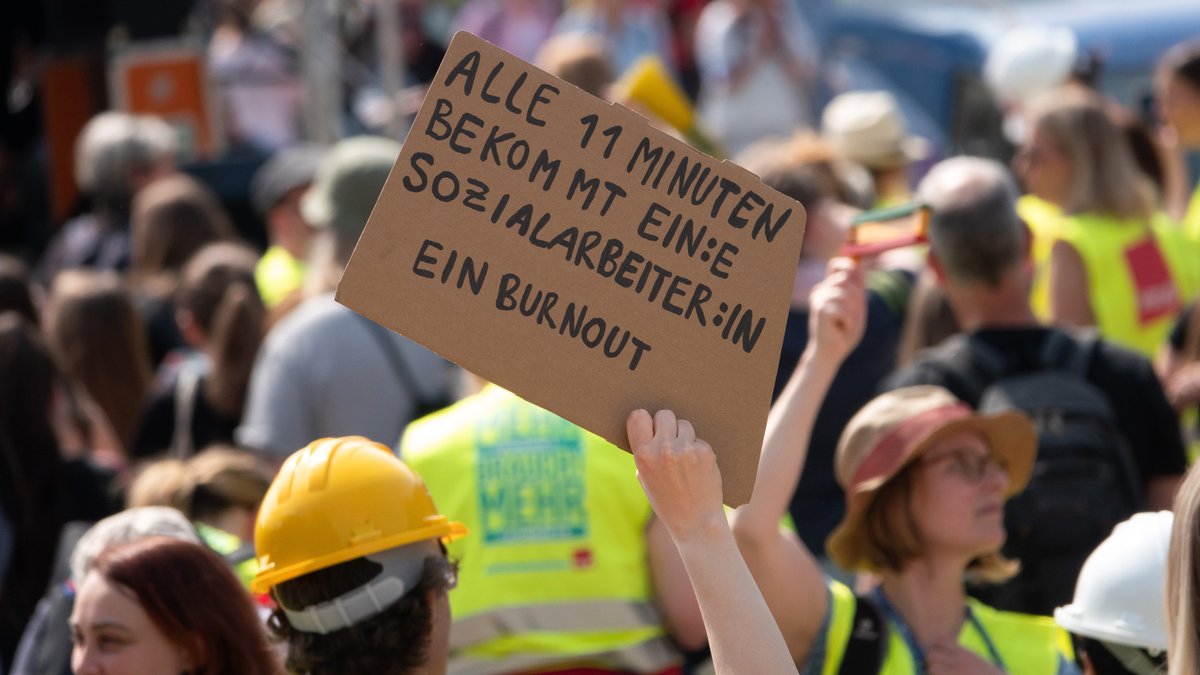 Eine Frau hält ein Schild mit der Aufschrift "Alle 11 Minuten bekommt ein:e Sozialarbeiter:in ein Burnout" auf einer Kundgebung mehrerer Gewerkschaften. (Archivbild)