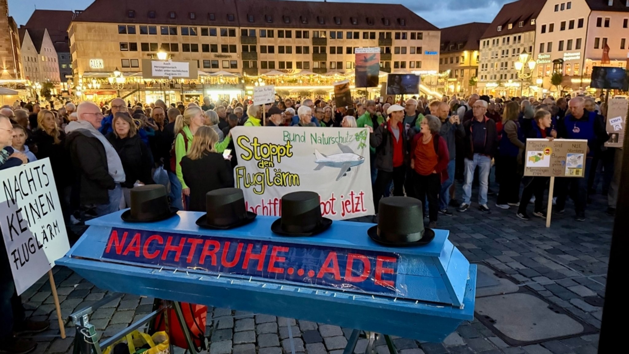 Auf dem Hauptmarkt Nürnberg stehen zahlreiche Demonstranten, im Vordergrund sieht man einen Sarg mit der Aufschrift "Nachtruhe ade". | Bild: BR / Michael Reiner Auf dem Hauptmarkt Nürnberg stehen zahlreiche Demonstranten, im Vordergrund sieht man einen Sarg mit der Aufschrift "Nachtruhe ade".