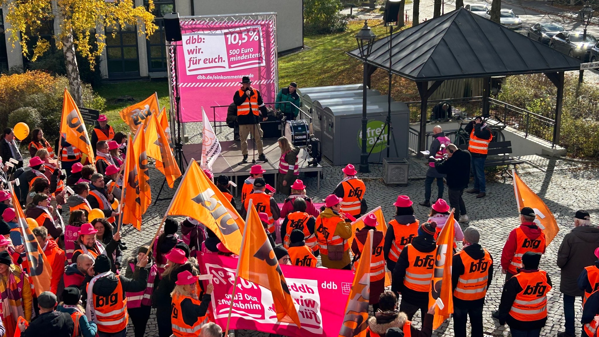 Teilnehmende einer Kundgebung stehen in orangenen Westen vor einem Rednerpult in Wunsiedel.