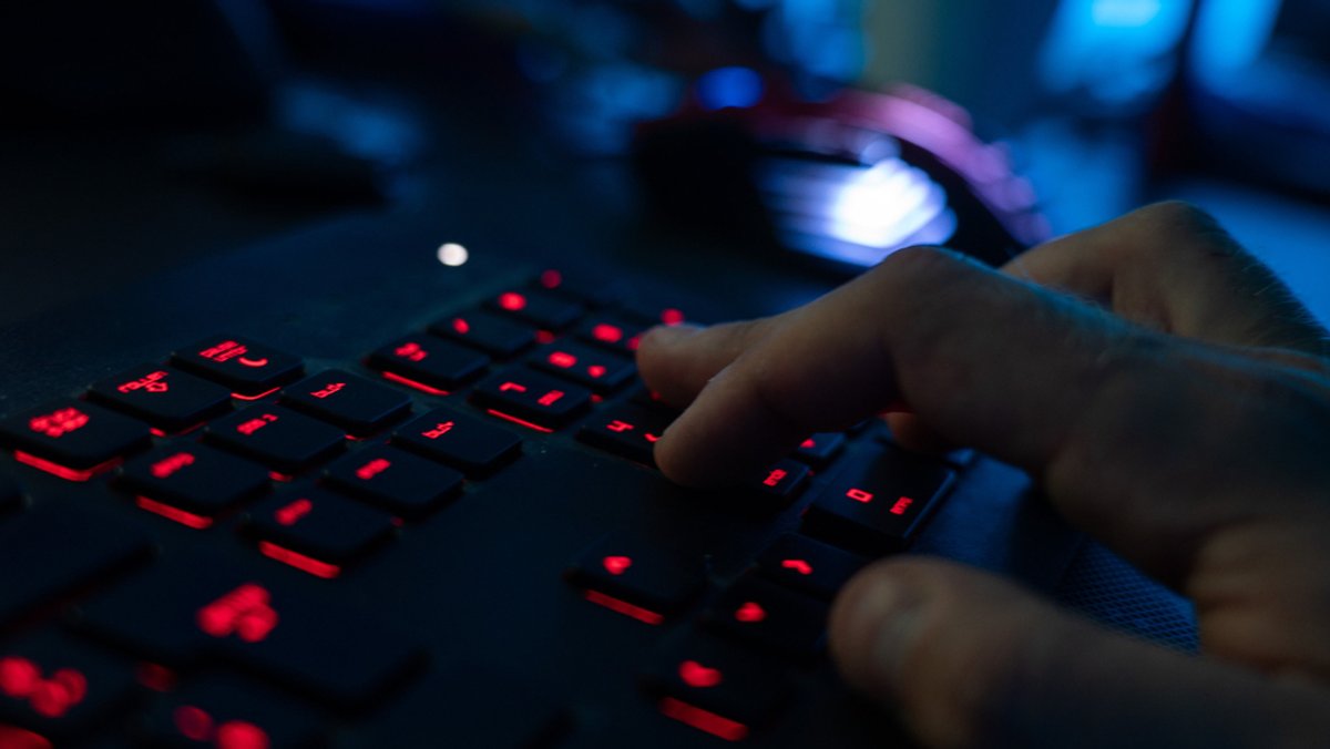 Eine Hand tippt auf einer rot beleuchteten Computertastatur. 