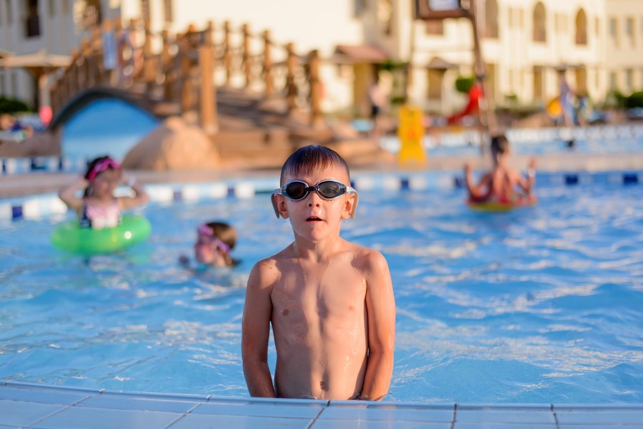 Junge mit Schwimmbrille steht im Schwimmbad im Becken