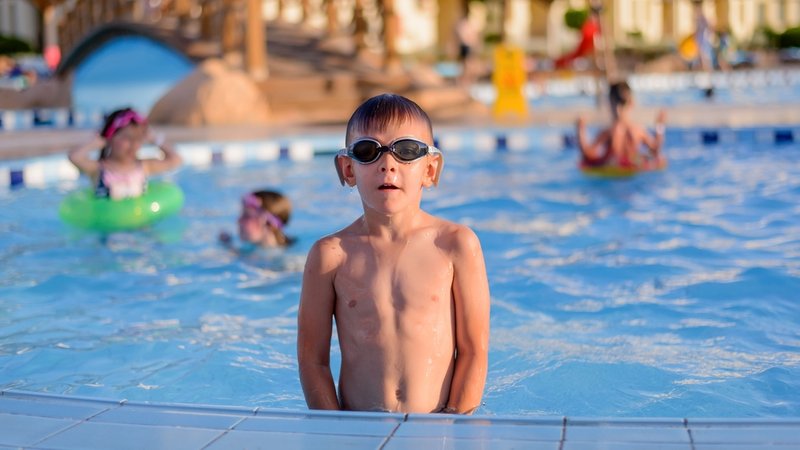 Junge mit Schwimmbrille steht im Schwimmbad im Becken