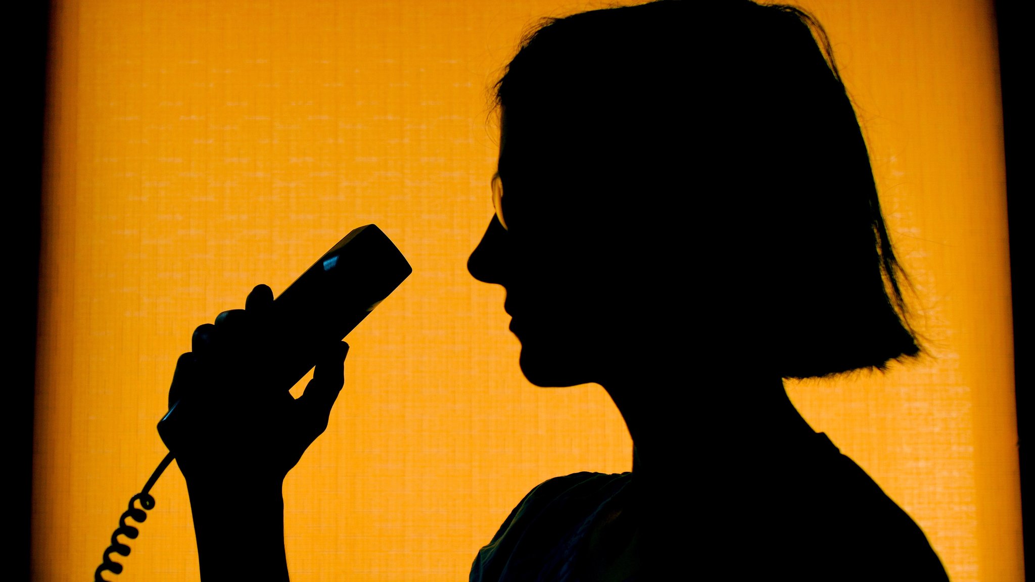 Silhouette einer Frau, die einen Telefonhörer hält, gegen gelbes Licht. 