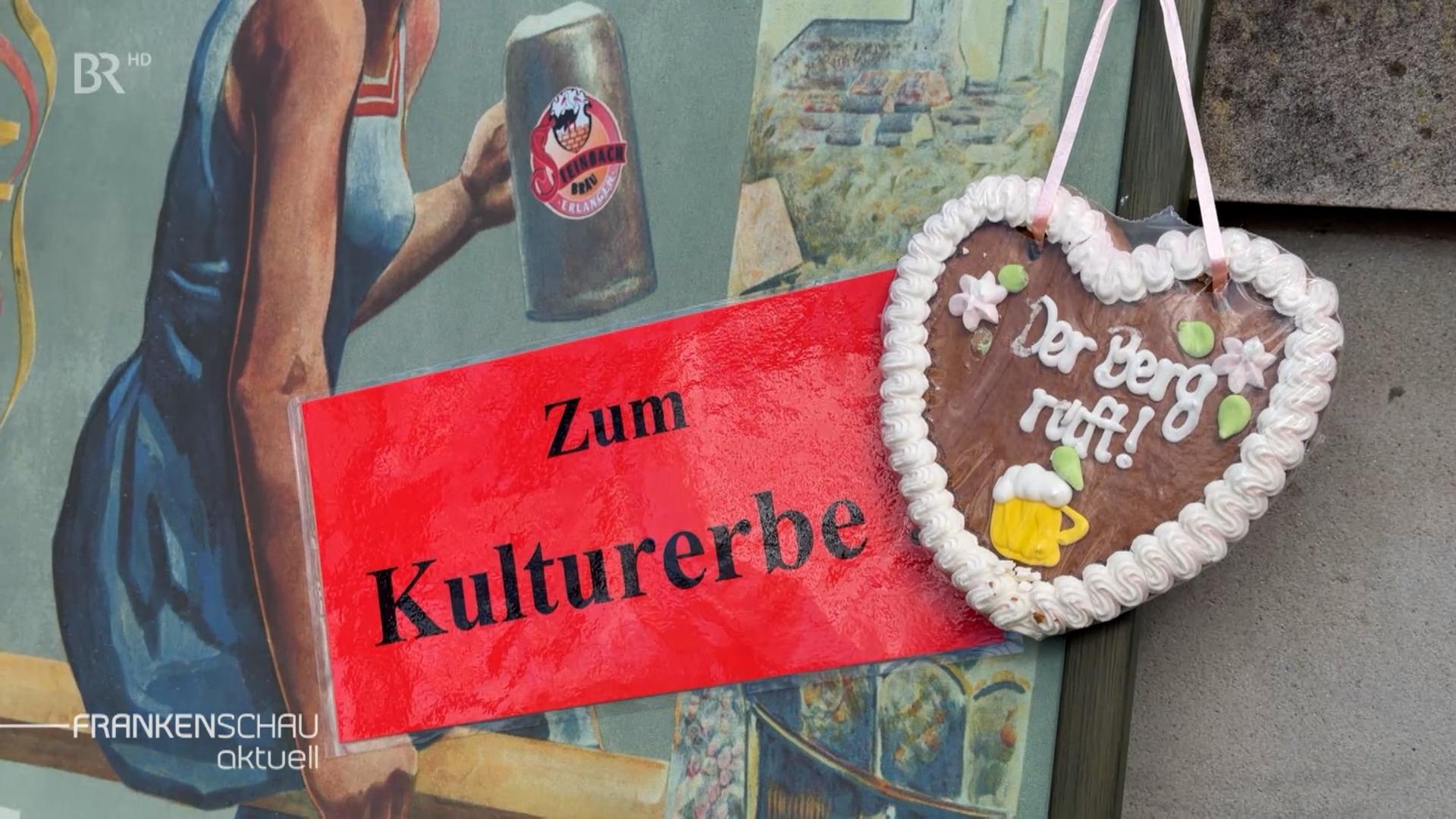 Schild mit Text "Zum Kulturerbe" neben einem Lebkuchenherz mit dem Text "Der Berg ruft".