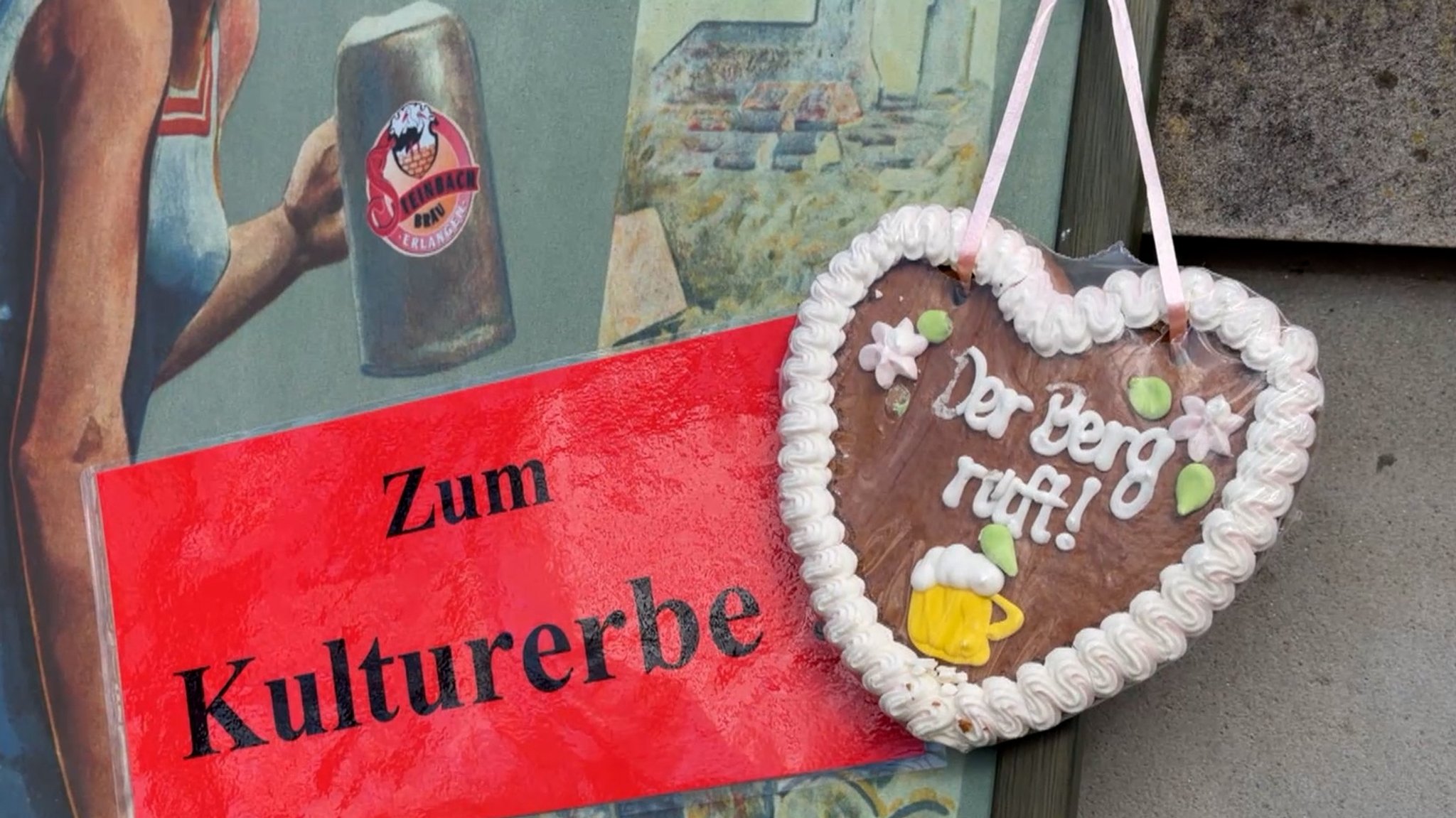Schild mit Text "Zum Kulturerbe" neben einem Lebkuchenherz mit dem Text "Der Berg ruft".