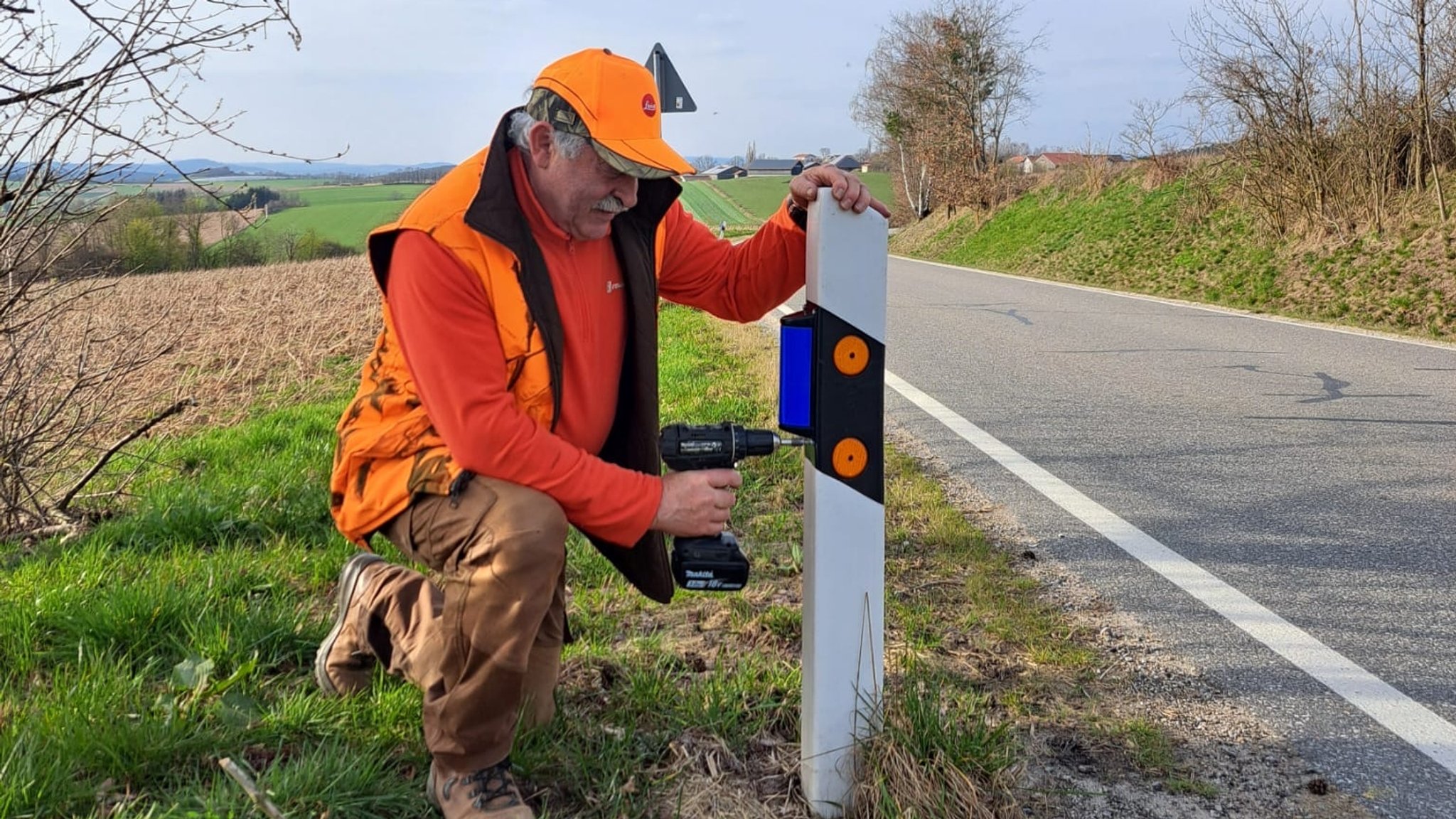 Jäger Gerhard Luckner aus Cham beim Montieren eines blauen Wildwarnreflektors an einem Leitpfosten.