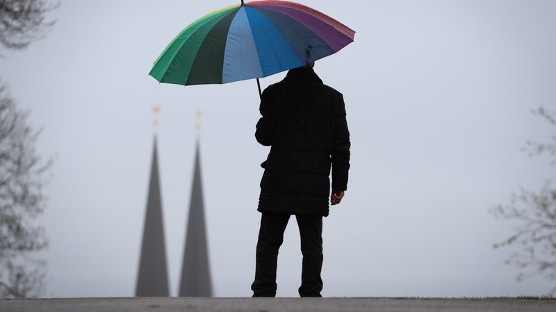 Mann mit Regenschirm im Herbst - im Hintergrund sind zwei Kirchtürme zu sehen (Symbolbild)