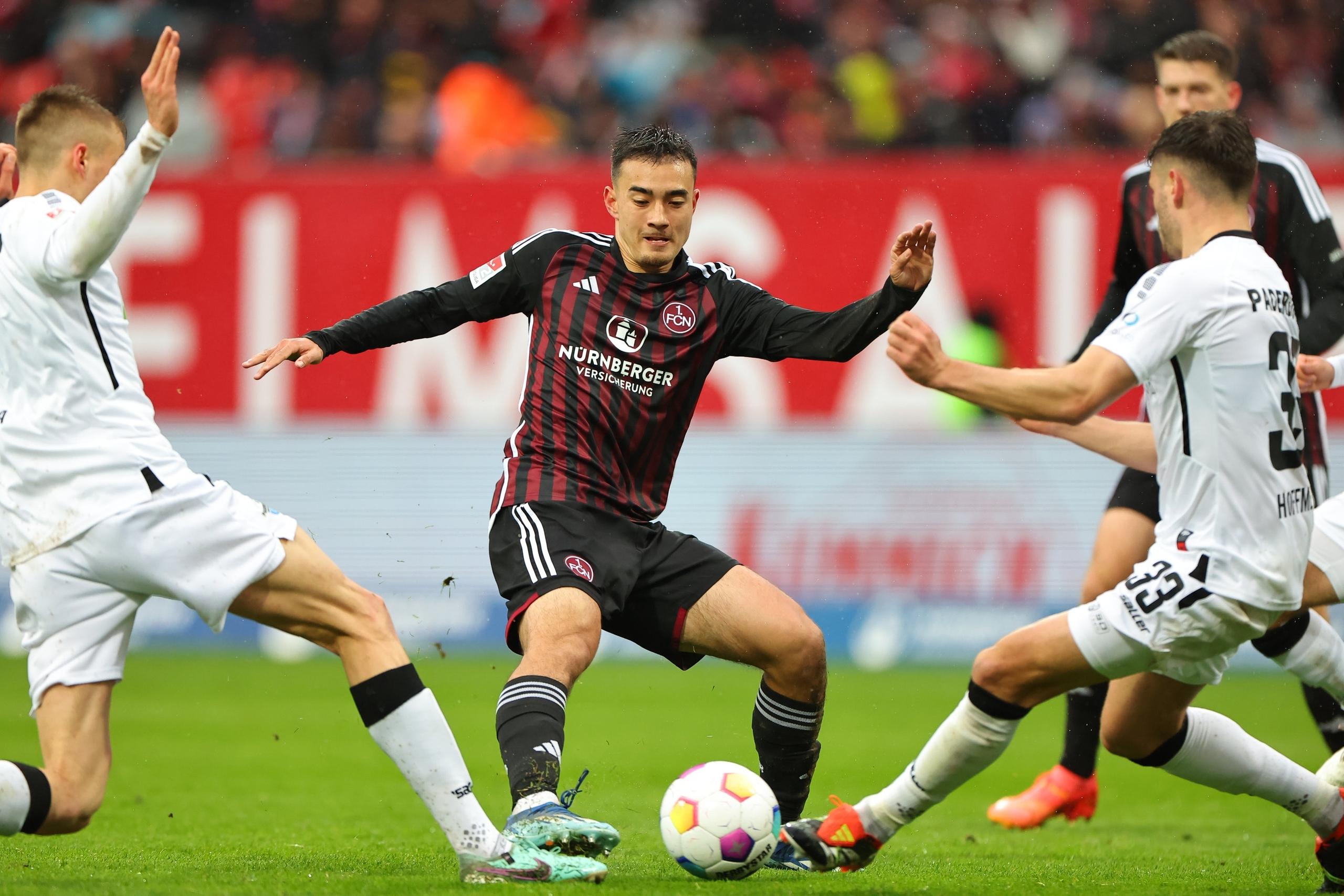 19.04.2024, Bayern, Nürnberg: Fußball: 2. Bundesliga, 1. FC Nürnberg - SC Paderborn 07, 30. Spieltag im Max-Morlock-Stadion. Der Nürnberger Jens Castrop (M) kämpft mit Filip Bilbija (l) und Marcel Hoffmeier aus Paderborn um den Ball. Foto: Daniel Karmann/dpa - WICHTIGER HINWEIS: Gemäß den Vorgaben der DFL Deutsche Fußball Liga bzw. des DFB Deutscher Fußball-Bund ist es untersagt, in dem Stadion und/oder vom Spiel angefertigte Fotoaufnahmen in Form von Sequenzbildern und/oder videoähnlichen Fotostrecken zu verwerten bzw. verwerten zu lassen. +++ dpa-Bildfunk +++