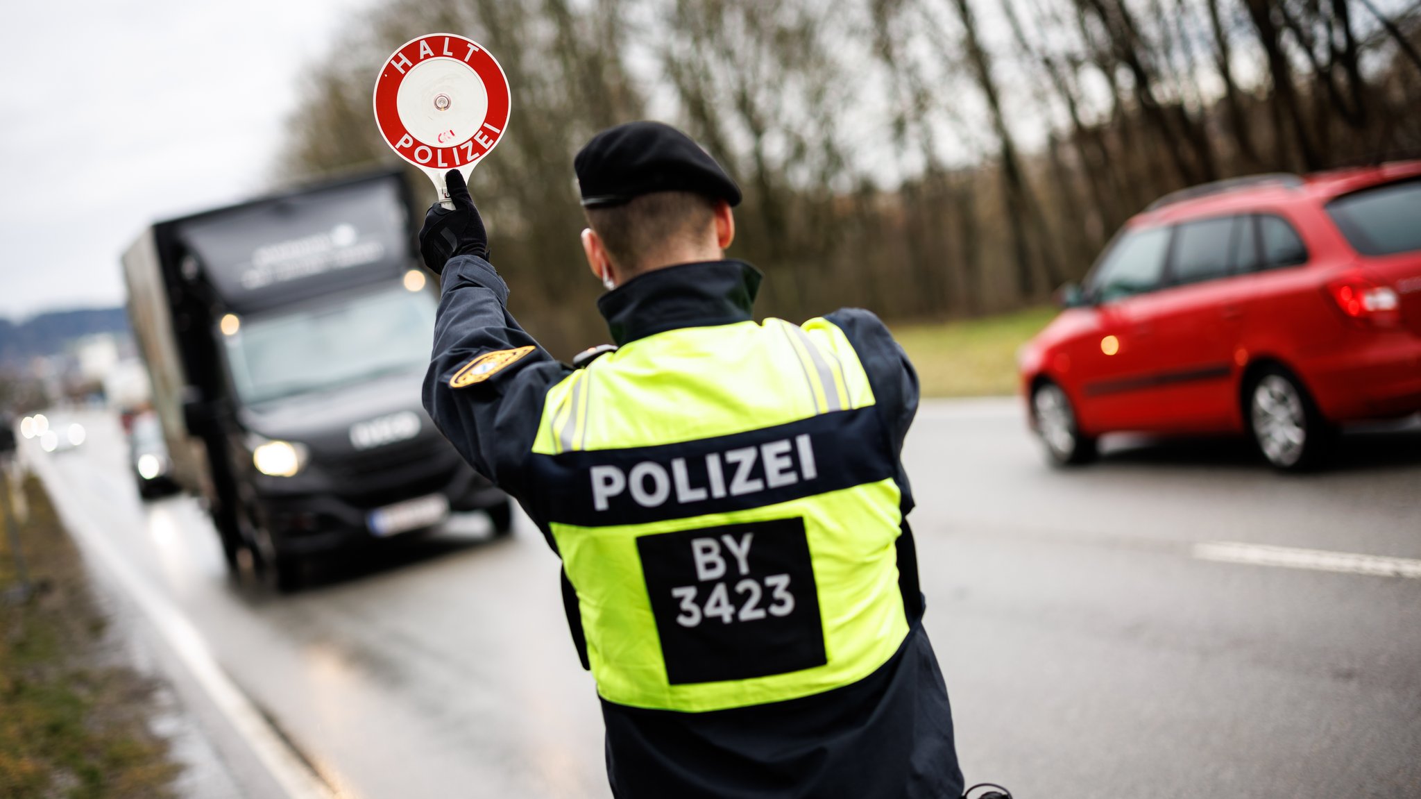 Ein Polizist zieht am 08.02.2024 an einer Kontrollstelle der bayerischen Grenzpolizei an der Grenze von Österreich nach Deutschland an der Bundesstraße 512 bei Neuhaus am Inn mit seiner Kelle mit der Aufschrift Halt Polizei einen Transporter aus dem Verkehr.