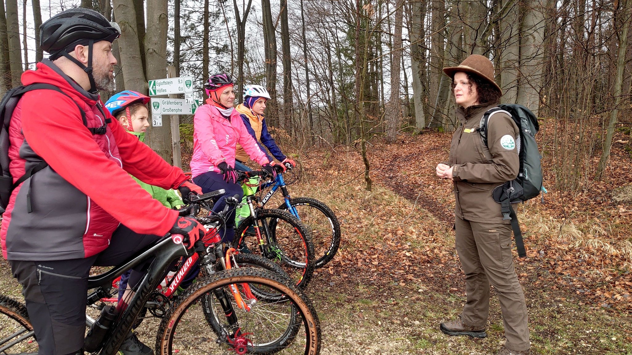 Naturparkrangerin Christine Berner erklärt einer Familie auf Rädern im Wald viel Wissenswertes über Flora und Fauna sowie deren Schutz.