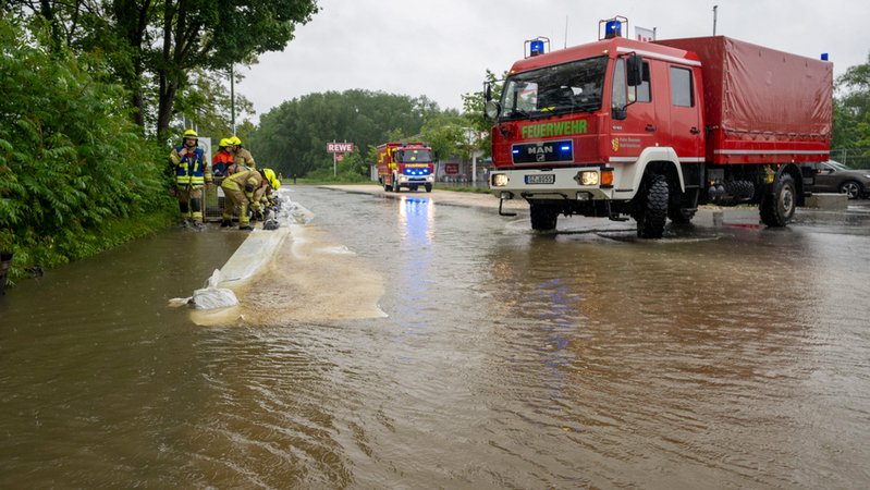 Feuerwehrleute errichten Barrieren an einer überfluteten Straße, um das Wasser aus der Stadt fernzuhalten.