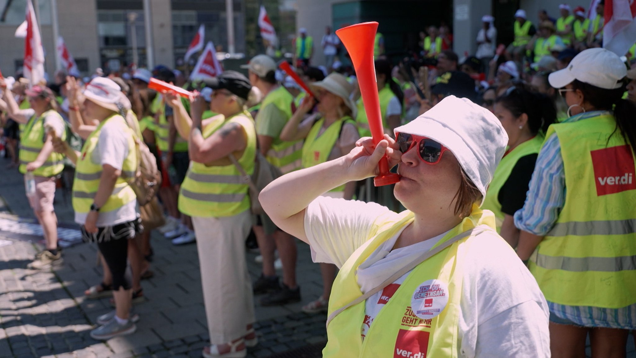 Streikende mit Tröten, gelben Westen und Sonnenschutz
