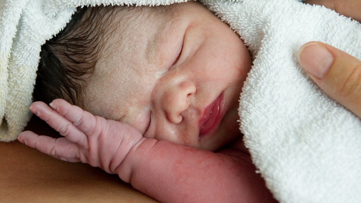 Ein neugeborenes Baby liegt nach der Geburt auf der Brust seine Mutter.