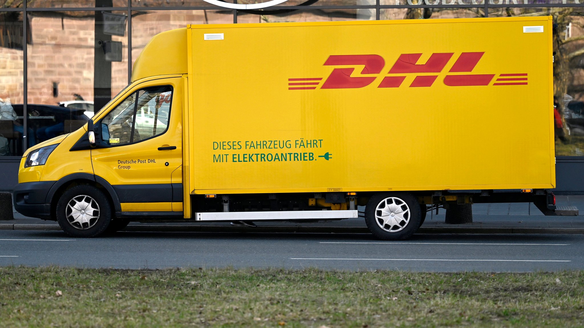 (Symbolbild) Ein gelbes Lieferauto der Post mit rotem DHL-Schriftzug parkt an einer Straße.