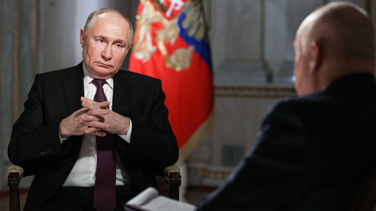 Der russische Präsident faltet die Hände vor einer Flagge