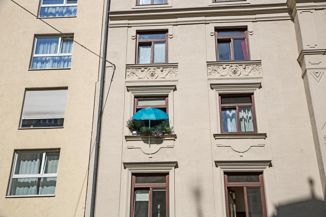 Die Fassade eines Wohnhauses in München. Ein Fenster ist mit vielen Blumentöpfen begrünt, darüber ein blauer Sonnenschirm
