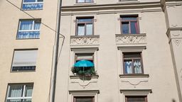 Die Fassade eines Wohnhauses in München. Ein Fenster ist mit vielen Blumentöpfen begrünt, darüber ein blauer Sonnenschirm | Bild:BR/Herbert Ebner