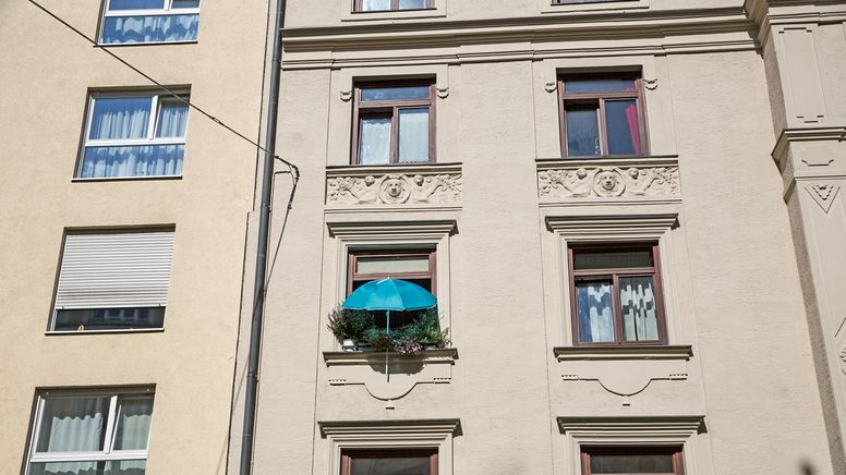 Die Fassade eines Wohnhauses in München. Ein Fenster ist mit vielen Blumentöpfen begrünt, darüber ein blauer Sonnenschirm | Bild:BR/Herbert Ebner