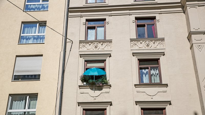 Die Fassade eines Wohnhauses in München. Ein Fenster ist mit vielen Blumentöpfen begrünt, darüber ein blauer Sonnenschirm