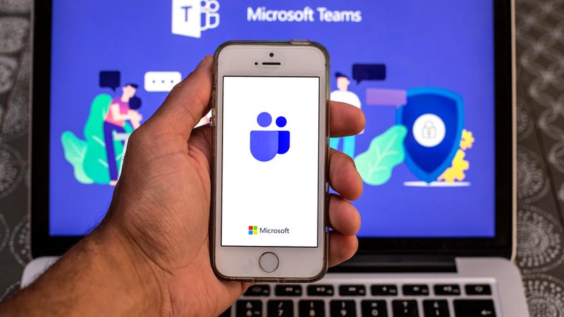 Microsoft-Teams-App auf einem Smartphone, im Hintergrund ein Laptop (Symbolbild)