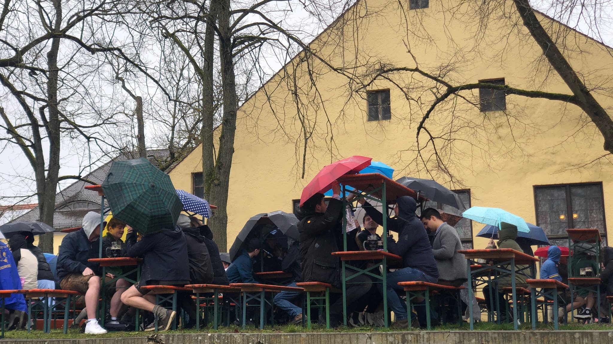 Besucher am Adlersberger Palmator auf Bierbänken unter Regenschirmen sitzend