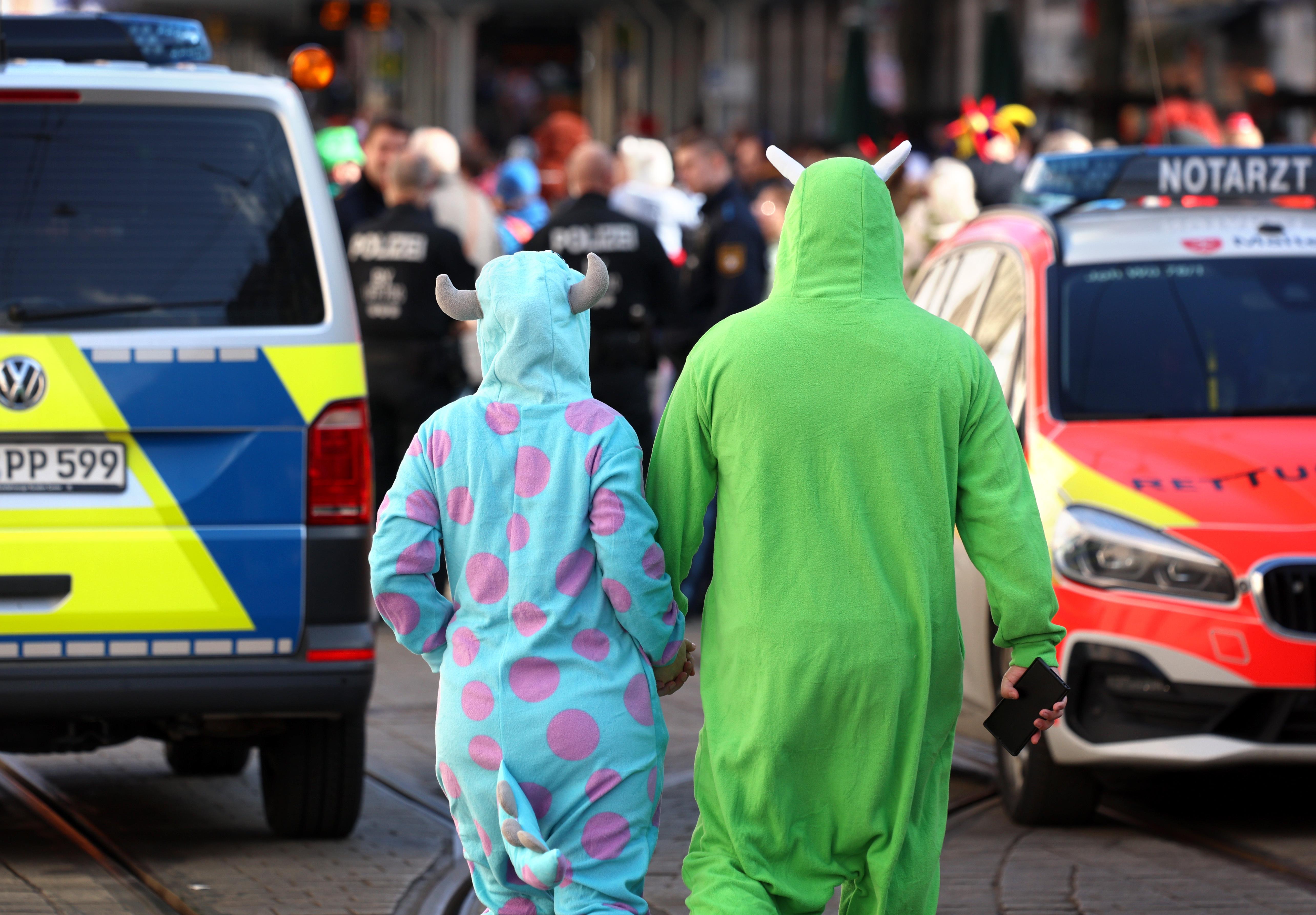 Verkleidete Besucher eines Faschingszuges laufen zwischen einem Polizei- und einem Notarztwagen.
