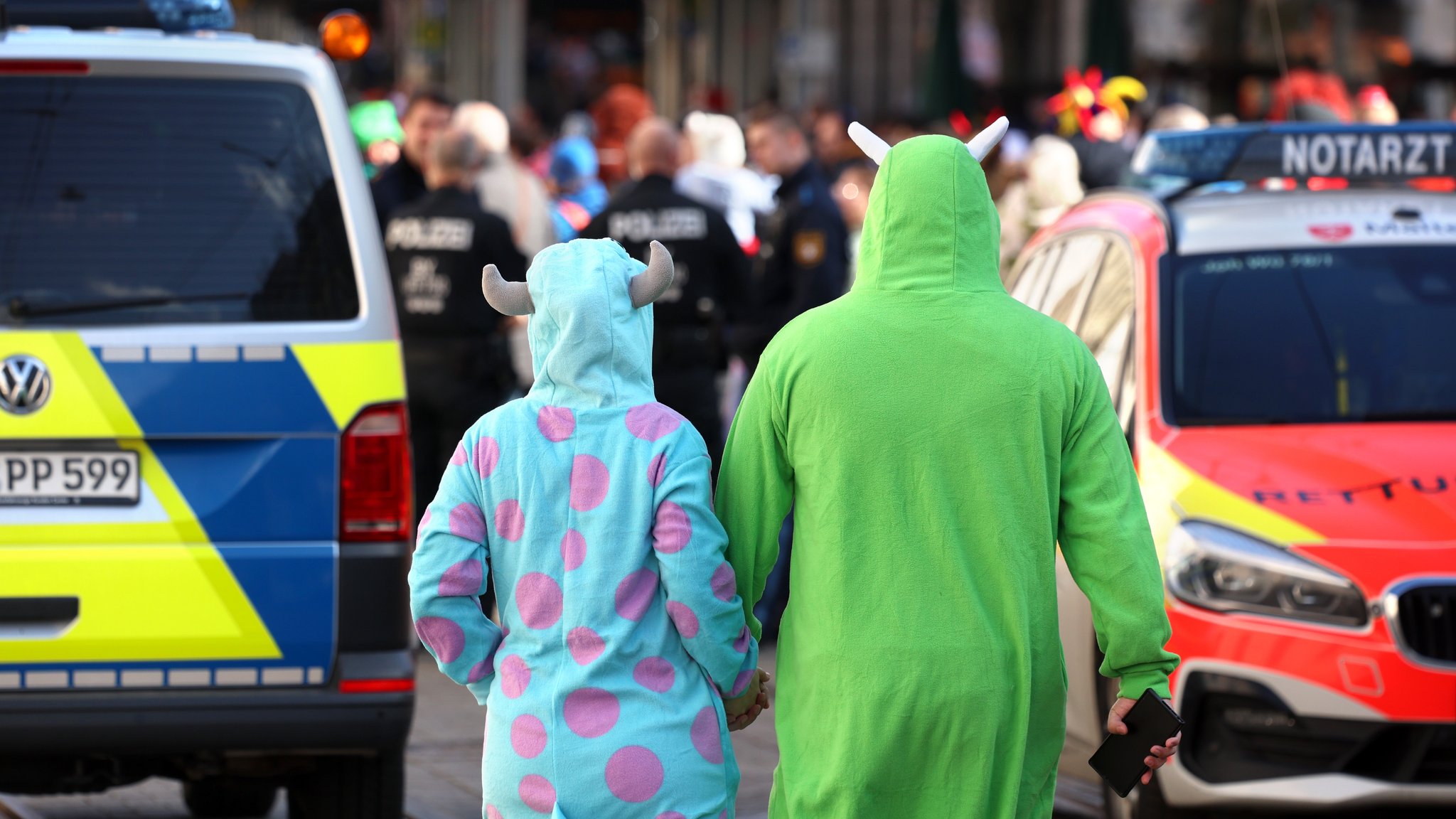 Verkleidete Besucher eines Faschingszuges laufen zwischen einem Polizei- und einem Notarztwagen.