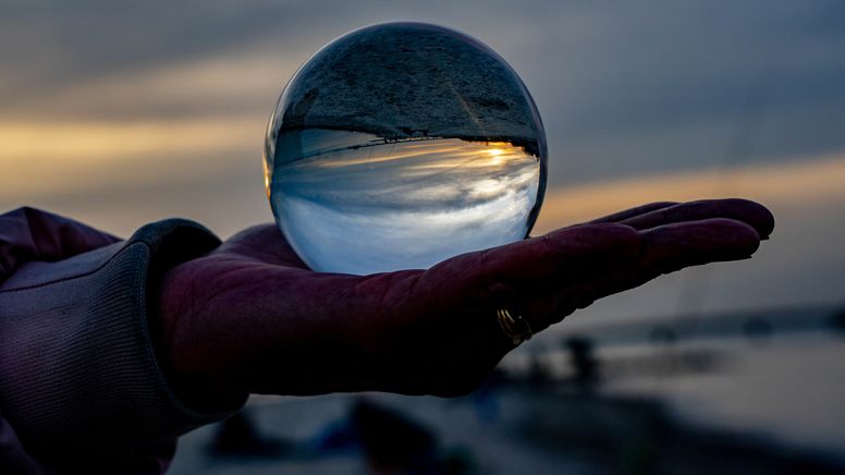 Foto: Eine Hand hält eine Glaskugel auf der Handfläche, darin spiegeln sich der Himmer und die Dämmerung. | Bild:dpa-Bildfunk/Axel Heimken