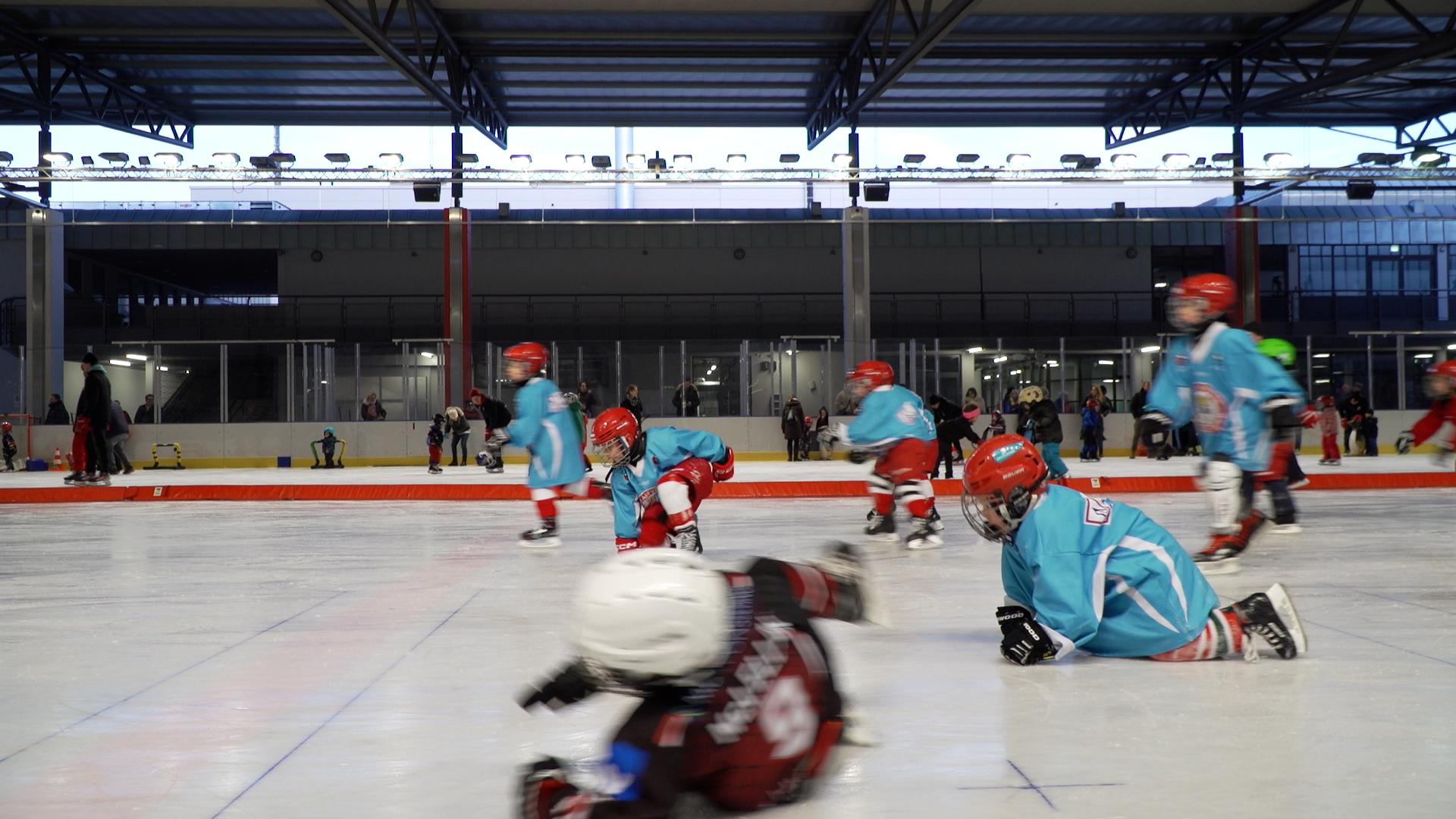 Kinder in Eishockeyausrüstung fallen auf das Eis.