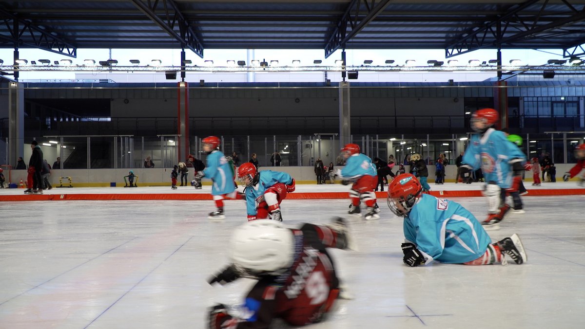 Kinder in Eishockeyausrüstung fallen auf das Eis.