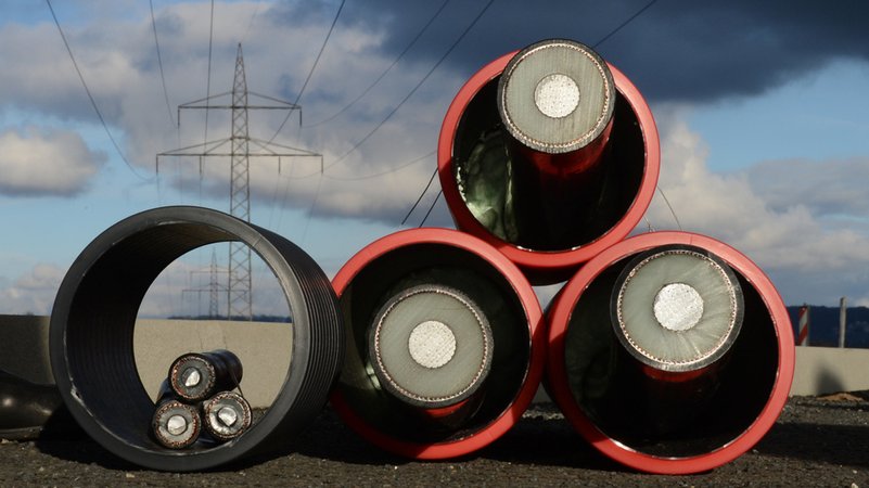 Zwei Prototypen für Erdkabel mit drei Adern liegen unter einer Hochspannungsleitung. | Bild: dpa-Bildfunk/Julian Stratenschulte Zwei Prototypen für Erdkabel mit drei Adern liegen unter einer Hochspannungsleitung.