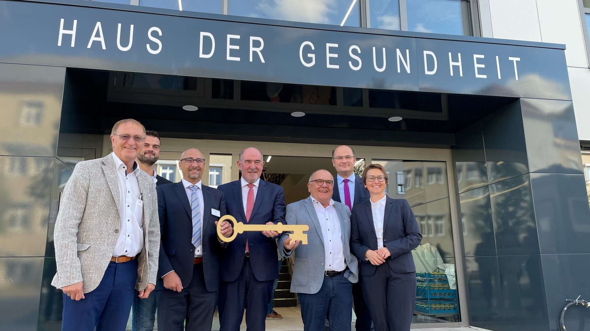 Menschen stehen vor dem Haus der Gesundheit und halten einen großen goldenen Schlüssel.