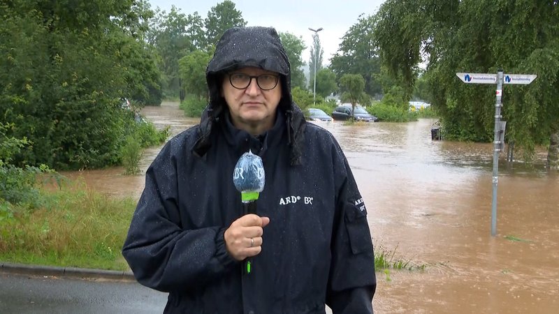 BR-Korrespondent Michael Reiner in Neustadt an der Aisch, im Hintergrund ein über die Ufer getretener Fluss